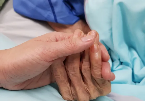 A hand gently holding an elderly person's hand